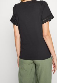 Svart t-shirt med korta, puffade ärmar som har en scallop-lace kant, matchad med lösa olivgröna byxor. Slät textur, avslappnad passform.