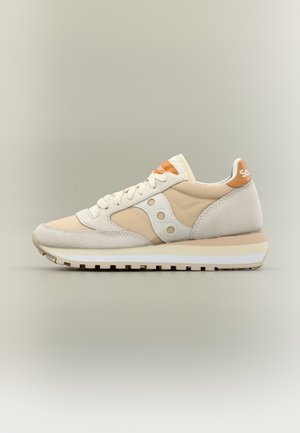 Beige en gebroken witte suède en stof hardloopschoen met witte zool en oranje logo op de tong en hiel, gezien van opzij.