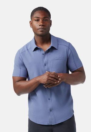 Short-sleeve, button-up shirt in light blue fabric, featuring a chest pocket, collar, and contrasting stitching details.