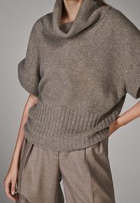 Lyhythihainen neulepaita, jossa on kaulus ja lämmin harmaa neulos, varustettuna resorireunuksella ja sileällä pinnalla, yhdistetty leveälahkeisiin vaaleanharmaisiin housuihin.