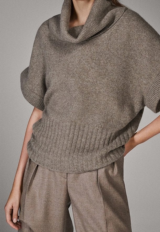 Lyhythihainen neulepaita, jossa on kaulus ja lämmin harmaa neulos, varustettuna resorireunuksella ja sileällä pinnalla, yhdistetty leveälahkeisiin vaaleanharmaisiin housuihin.