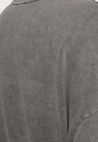 Tessuto morbido e grigio lavorato a maglia che mostra dettagliati texture e cuciture sull'area della spalla e della schiena di un capo.