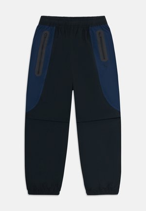 Schwarze und marineblaue Sporthosen mit elastischem Bund und Bündchen sowie seitlichen Reißverschlusstaschen, die mit reflektierenden Details umrandet sind.