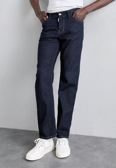 Dunkelblaue Denim-Jeans mit geradem Bein, ausgestattet mit fünf Taschen und dezenten gelben Nähten. Kombiniert mit weißen Sneakern.