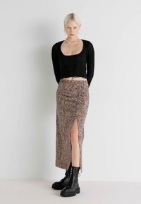 Jupe maxi en imprimé léopard avec une fente haute, fabriquée en tissu doux. Associée à un haut ajusté à manches longues noir et des bottes de combat noires.