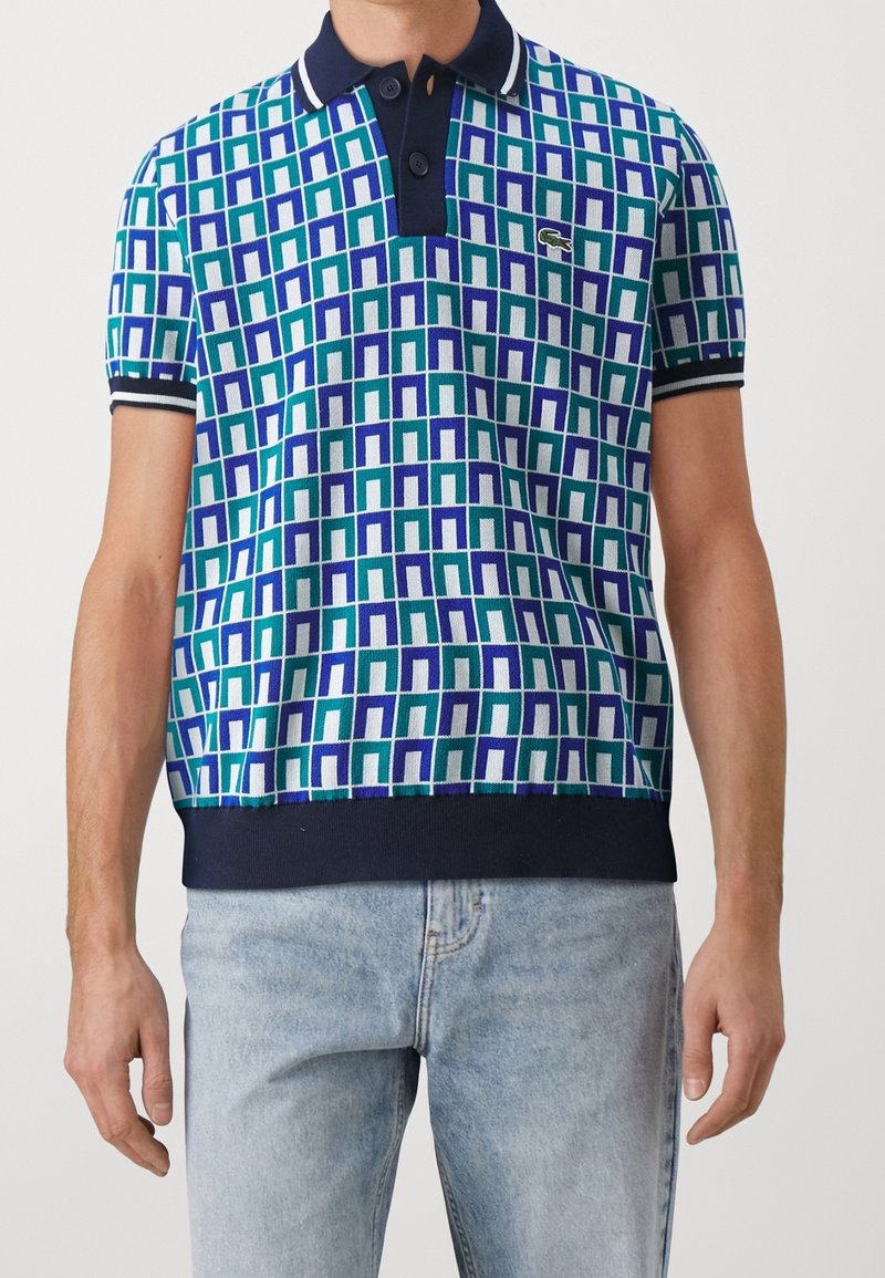 Kortärmad polo med rutmönster i grön, blå och vit. Marinblå krage och ärmslut, med två knappar och en logotyp på bröstet.