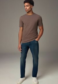 Camiseta marrón de manga corta combinada con vaqueros azules y zapatillas blancas. La camiseta tiene un escote redondo y un diseño ajustado.