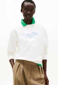 Witte sweatshirt met groene kraag, voorzien van het 'Tommy Hilfiger' logo in lichtblauw, in combinatie met crèmekleurige plissébroek.