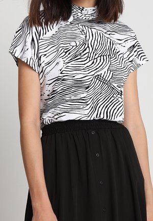 Kvinde iført en hvid top med korte ærmer med sorte abstrakte zebra-striber og et sort højtaljet skørt med knapper.