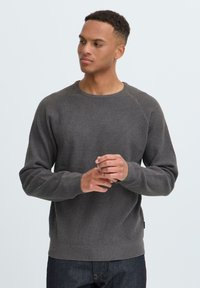 Grå teksturert genser med rund hals og raglanermer, med en ribbestrikket kant og mansjetter. Brukt med mørkeblå jeans.
