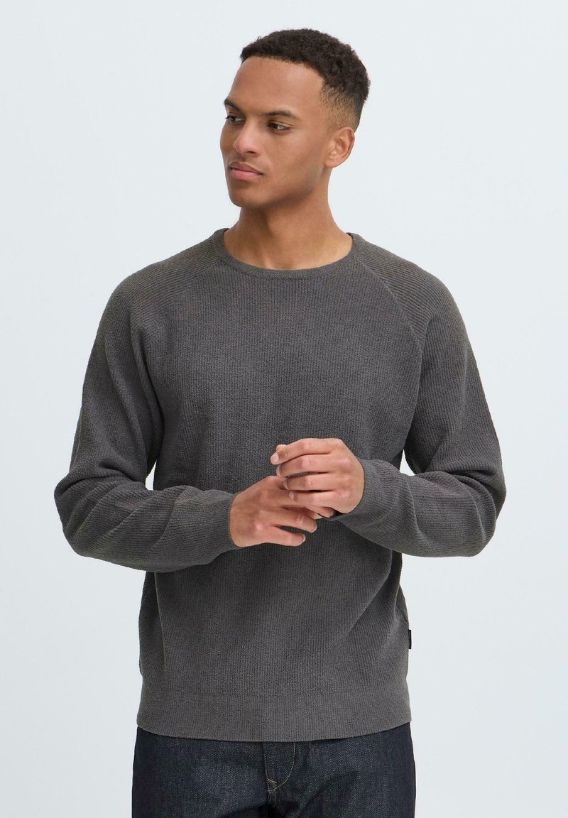 Grå teksturert genser med rund hals og raglanermer, med en ribbestrikket kant og mansjetter. Brukt med mørkeblå jeans.