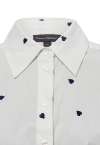 White shirt with a classic collar, featuring navy blue heart-shaped embroidery. Button closure with pearl-like buttons. Size label visible.