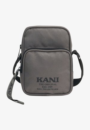 Grå lærred crossbody taske med to lynlåslommer foran, justerbar rem og sort trykt logotekst foran. Kompakt og struktureret design.