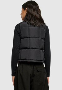 Svart boblevest med quiltet design, med en cropped lengde og justerbar kant. Båret over en langermet topp med teksturert finish.
