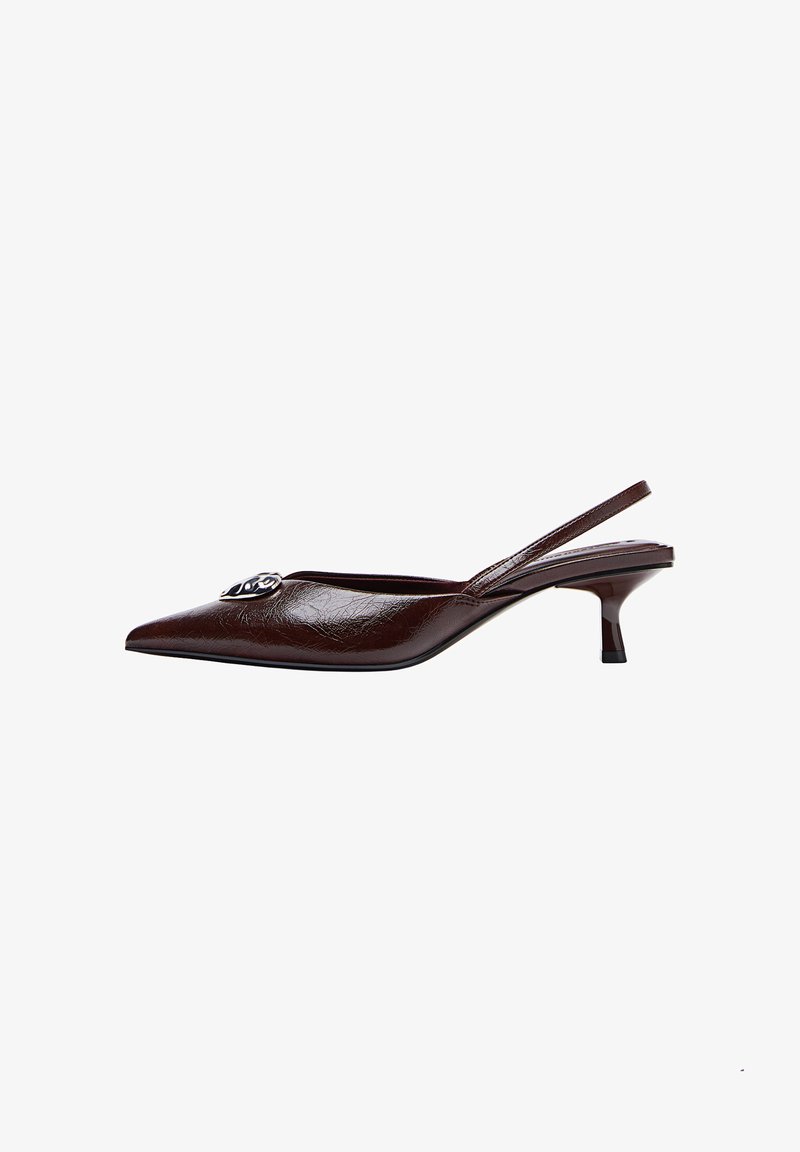 Temno rjave slingback čevlje s koničastim prstom in peto kitten ter s srebrnim dekorativnim emblemom na zgornjem delu, postavljeni na belo ozadje.