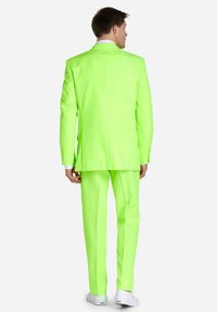 Neon grüner Anzug mit taillierter Passform; verfügt über einen einzelnen Rückenschlitz und passende Hosen, kombiniert mit weißen Sneakers.