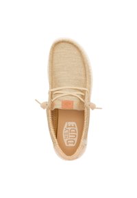 Zapatilla de tela beige con parte superior texturizada, cordones elásticos y parche con logo en el talón. Presenta una suela suave y flexible para mayor comodidad.