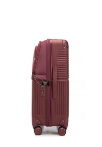 Valigia rigida di colore rosso scuro con texture a righe, ruote doppie per la mobilità, chiusura a combinazione e zip lungo il lato.
