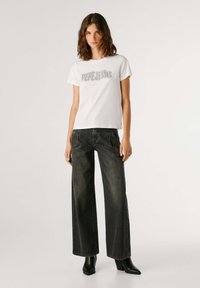 Camiseta blanca con logo gris "PEPE JEANS", combinada con vaqueros de pierna ancha de mezclilla oscura de cintura alta y botines negros de tacón.