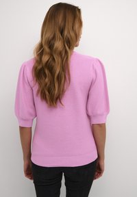 Haut en maille rose ajusté avec manches courtes bouffantes, ourlet côtelé et texture structurée, vu de dos sur un fond uni.