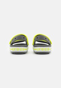 Harmaat ja neonkeltaiset Crocsit, joissa on takanauha, ilmanvaihtoaukot ja valkoinen logonauha, jossa on kaksi keltaista raitaa. Kumia.