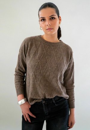 Pull en tricot marron avec un motif en losange, col rond et poignets côtelés. Associé à un jean foncé et un bracelet en argent.