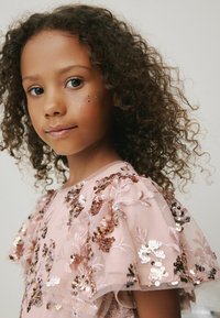 Pink kjole med pailletter og blomsterbroderi, med flæseærmer og en blød tekstur, accentueret af glitrende dekorationer.