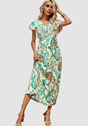 Una mujer lleva un vestido midi blanco con estampado floral y paisley, ribete de encaje, mangas cortas, un cinturón y sandalias de tacón alto en color marrón claro sobre un fondo liso.