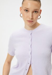 Kurze ärmelige Lavendel-Cardigan aus weichem, strukturiertem Material, mit rundem Halsausschnitt und sechs Knopfverschluss mit gewelltem Rand.