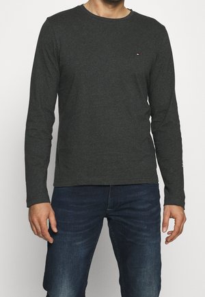 Tmavě šedá košile s dlouhým rukávem a kulatým výstřihem, vyrobená z měkké směsi bavlny. Na levé části hrudi se nachází malé logo.