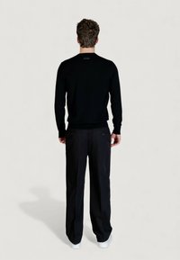 Maglione nero a maniche lunghe con scollo rotondo, abbinato a pantaloni scuri e sneakers bianche. Presenta un dettaglio con logo sul retro.