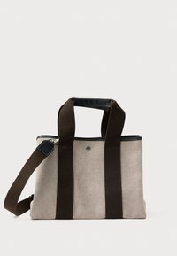 Plátěná taška v světle béžové barvě s tmavě hnědými rukojeťmi a ramenním popruhem. Má zipové uzavření a černé kožené detaily. Kompaktní design.