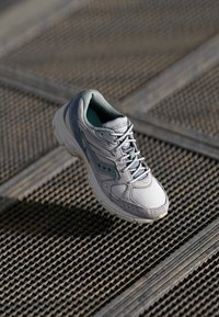 Baskets de sport gris clair avec une tige en maille texturée, un col rembourré et des accents verts. Semelle en caoutchouc avec un motif de traction visible.