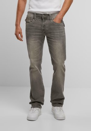 Jeans de mezclilla gris con un corte recto, ligera decoloración y costuras contrastantes. Llevados con zapatillas blancas y una camiseta blanca sencilla.