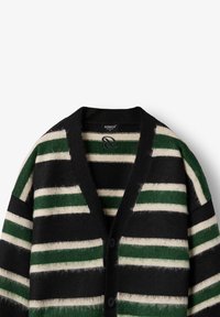 Melna kardigana ar vertikālām svītrām zaļā un baltā krāsā, izgatavota no mīksta materiāla. Ar V-veida kakla izgriezumu un divām melnām pogām priekšā.