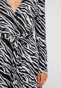 Czarna i szara sukienka w paski zebry, z długimi rękawami, głębokim dekoltem w kształcie litery V i wiązaniem w talii. Miękka tkanina o teksturowanym wzorze.