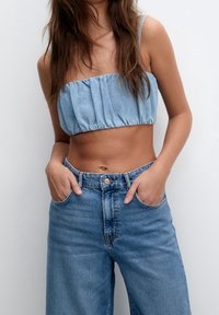 Haut court en denim avec détail froncé, couleur bleu clair. Associé à un jean bleu taille haute, coupe ample, avec poches avant et fermeture par bouton.