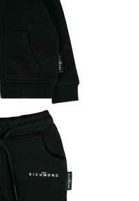 Zwarte katoenen rits hoodie met ribgebreide zoom, grote voorzak en merketiket. Een paar bijpassende zwarte joggingsbroeken met trekkoord en zijzakken.