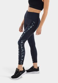 Leggings neri con una vita alta e un motivo a pannello testurizzato sui lati in grigio chiaro e accenti grigi scuri. Abbinati a scarpe sportive nere.