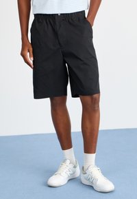 Svarte shorts med elastisk midje og lommer, sammen med hvite joggesko og lyse sokker. Enkel, strømlinjeformet design.