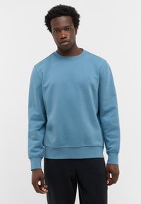 Jasnoniebieska bluza z miękkiego materiału. Posiada okrągły dekolt oraz ściągacze na rękawach. Mały detal logo na lewej piersi.