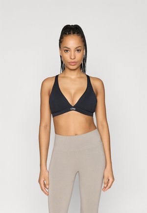 Svart trådlös bralette med djup V-ringning, slätt tyg och elastisk band med logotyp. Matchas med höga ljusgrå tights.