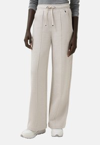 Beige weit geschnittene Sweatpants aus weichem Material, mit einem Kordelzugbund, seitlichen Nähdetails und einem lässigen Schnitt im Knöchelbereich.