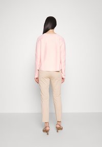 Pull rose clair à manches longues, col rond, et un dos légèrement plus long. Pantalon beige ajusté et escarpins légers à brides.