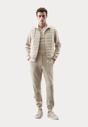 Beige, gewatteerde vest over een bijpassend trainingspak met een ritskraag en een taille met trekkoord. Beschikt over zachte stof en een eenvoudig ontwerp.