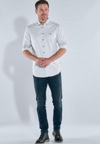 Weiß gestreiftes Hemd mit umgeschlagenen Ärmeln, kombiniert mit dunklen Jeans und schwarzen Ankle Boots. Mit einem dezenten Logo auf der Brust.