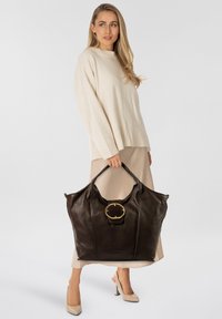 Borsa tote in pelle marrone con grande fibbia circolare dorata. Texture liscia, forma ampia e manici robusti per un facile trasporto.