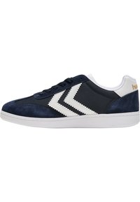 Marina mockasiner i sammet med vita detaljer, med snörning och en texturerad sula. Anmärkningsvärd chevronmönster på sidorna.