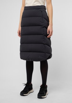 Black puffer skirt with horizontal quilted sections, mid-calf length, featuring side zippers and a logo patch at the hem. Worn with black shoes.