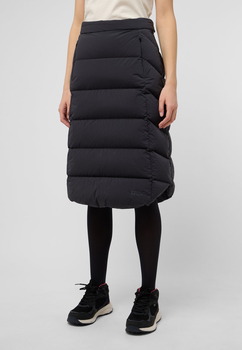 Zwarte pufferrok met horizontale gestikte secties, lengte tot halverwege het kuit, met zijritsen en een logo patch aan de onderrand. Gegdraagd met zwarte schoenen.